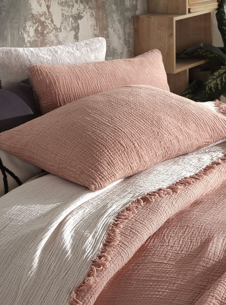 an unmade bed with pink linens and pillows