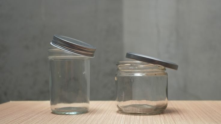 two glass jars with lids sitting on a wooden table next to each other and one has a metal lid