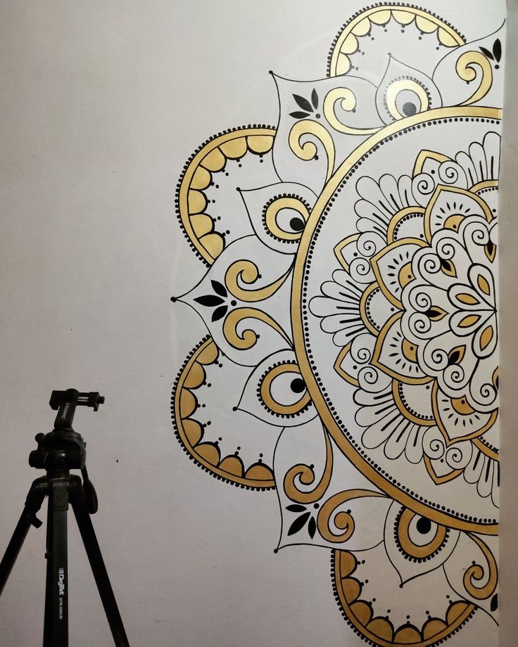 a tripod is sitting next to a wall with an ornate design on it and a camera in front of it