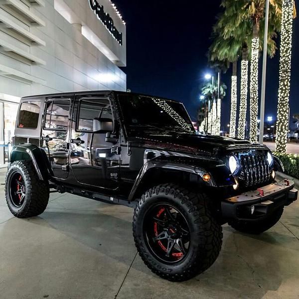 a black jeep parked in front of a building at night with palm trees behind it