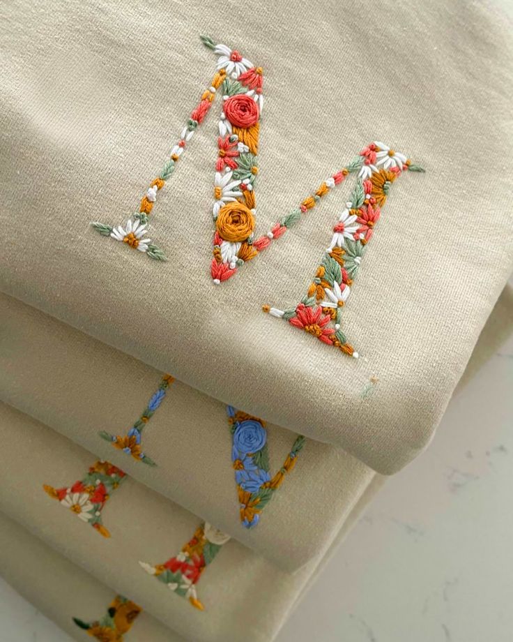 three pieces of cloth with embroidered letters on them, one in white and the other in orange