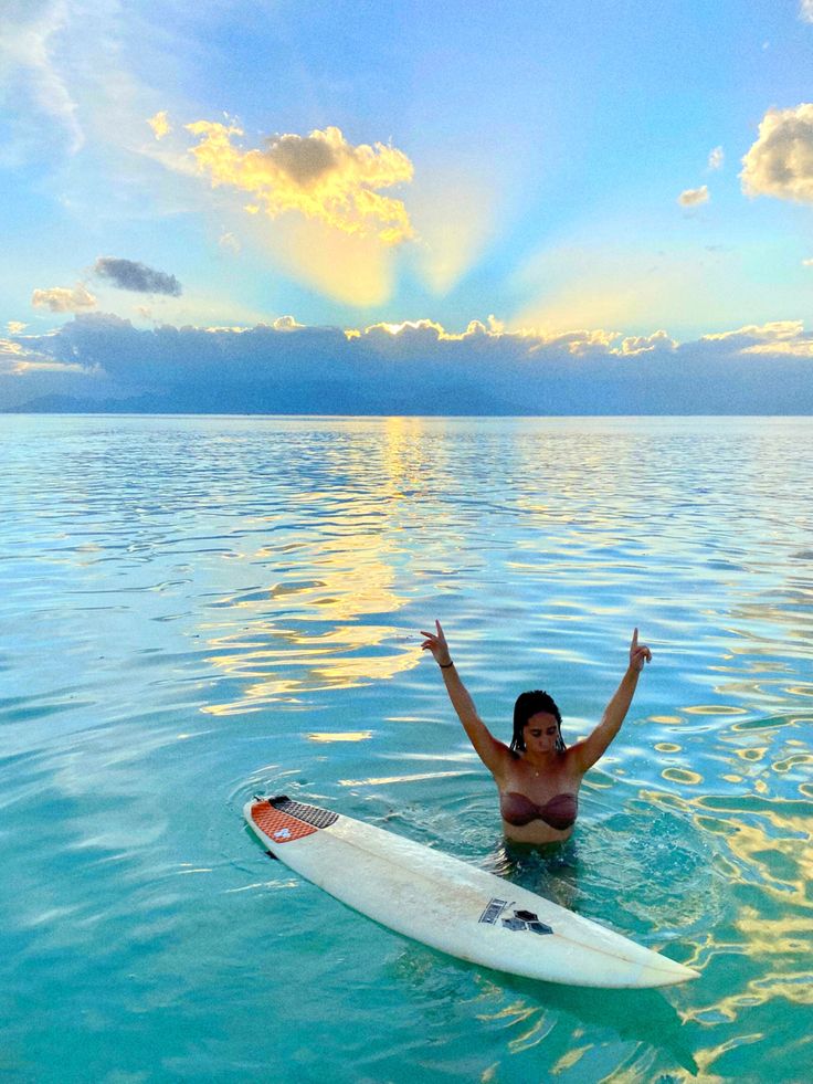 a woman on a surfboard in the ocean with her arms up and hands raised