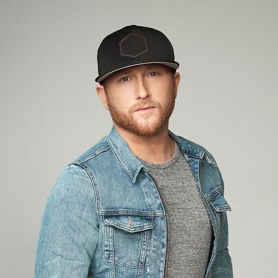 a man in a denim jacket and hat posing for the camera with his hands in his pockets