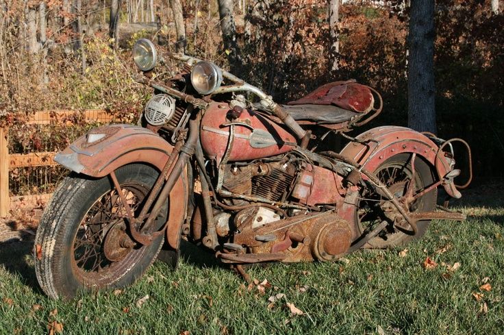 an old rusted out motorcycle sitting in the grass next to a fence and trees