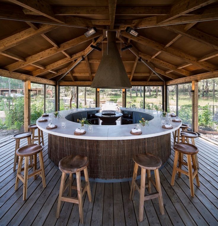 an outdoor hot tub with stools and tables in the center is surrounded by wood beams