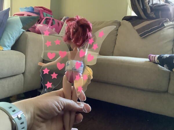 a hand holding a doll with pink stars on it's body and wings, in front of a couch