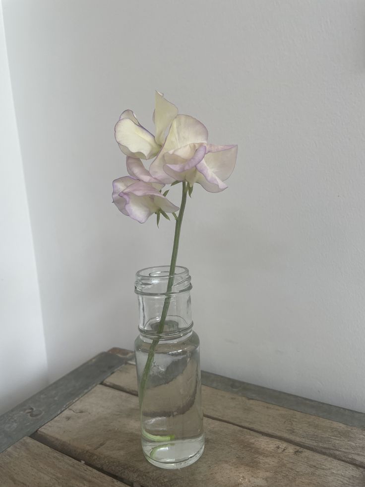 there is a glass vase with flowers in it on the wooden table next to a white wall