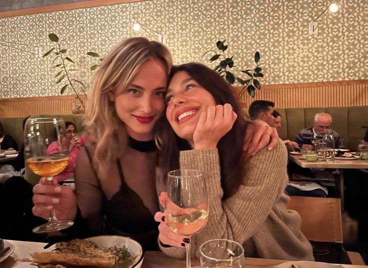 two women sitting at a table with food and wine glasses in front of their faces