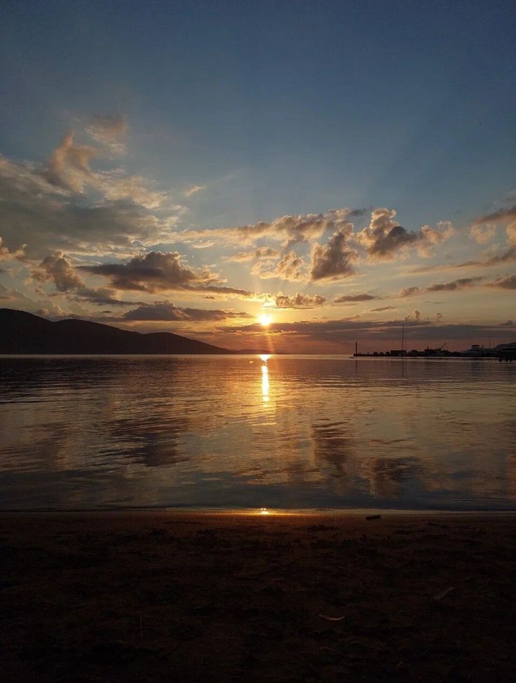 the sun is setting over the water and clouds are reflected in the still water on the beach