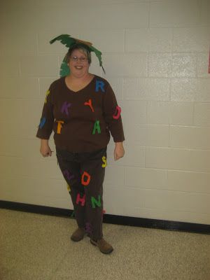 a woman dressed as a person with letters all over her body and head, standing in front of a wall