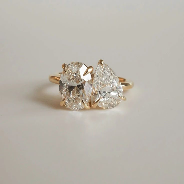 three pear shaped diamond engagement rings on a white surface with the top one in yellow gold