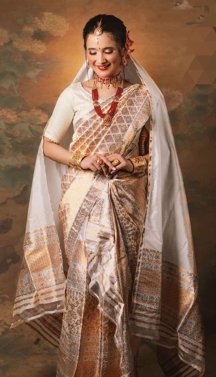 a woman in a white and gold sari is posing for the camera with her hands on her hips