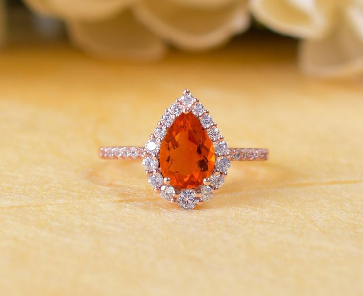 an orange and white diamond ring sitting on top of a wooden table next to flowers