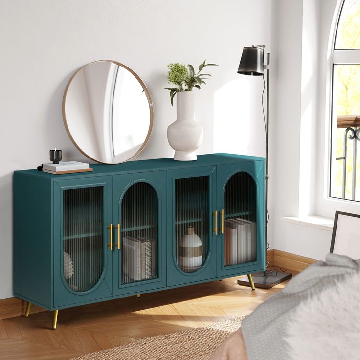 a blue cabinet with glass doors and gold handles next to a round mirror on the wall