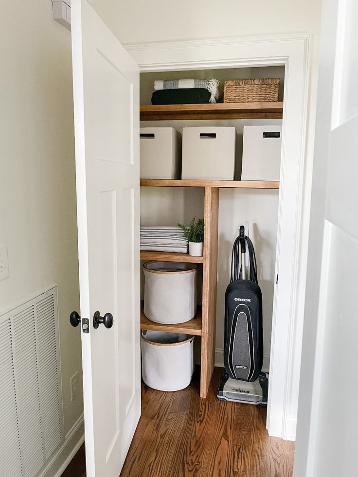 an open closet with several white containers and a black bag on the floor next to it