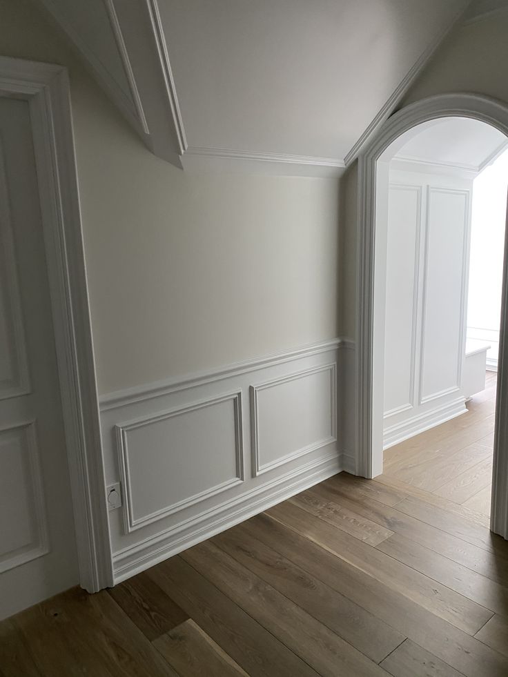 an empty room with white walls and wood floors, along with two doors leading to another room