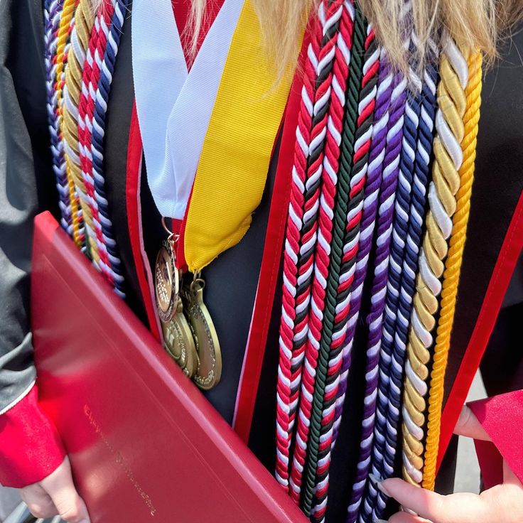 a woman wearing a graduation gown and holding a red folder with braids on it