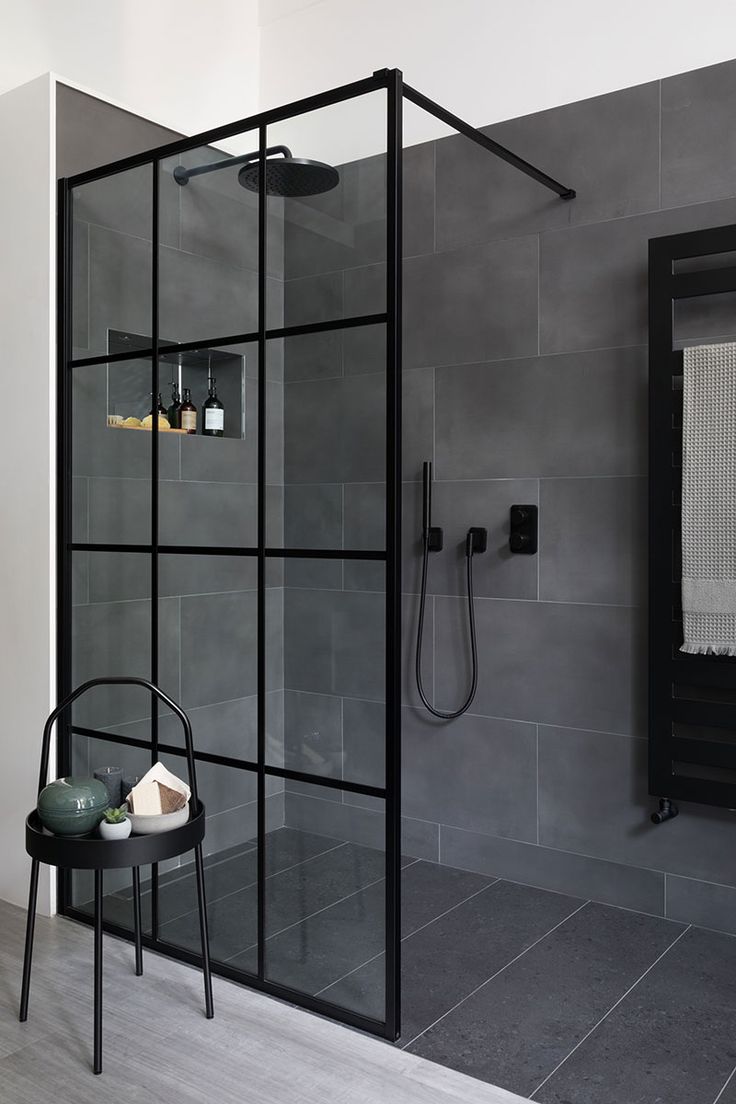 a black and white bathroom with glass shower door, grey tiled walls and flooring