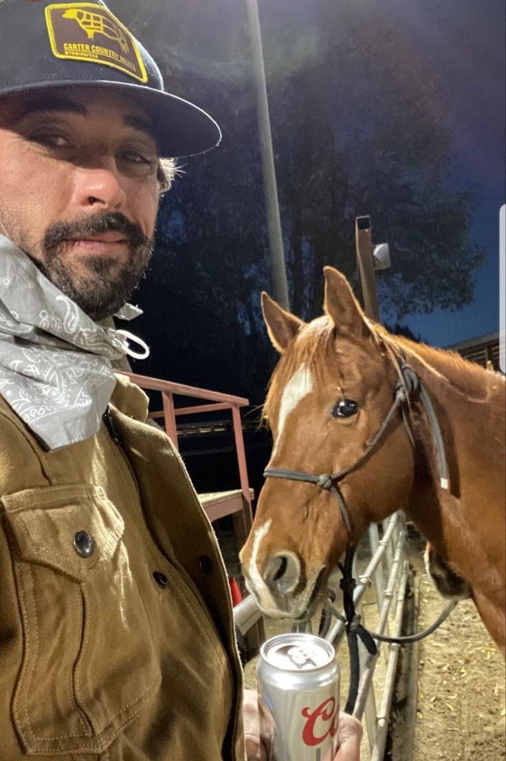 a man standing next to a brown horse with a can of beer in his hand