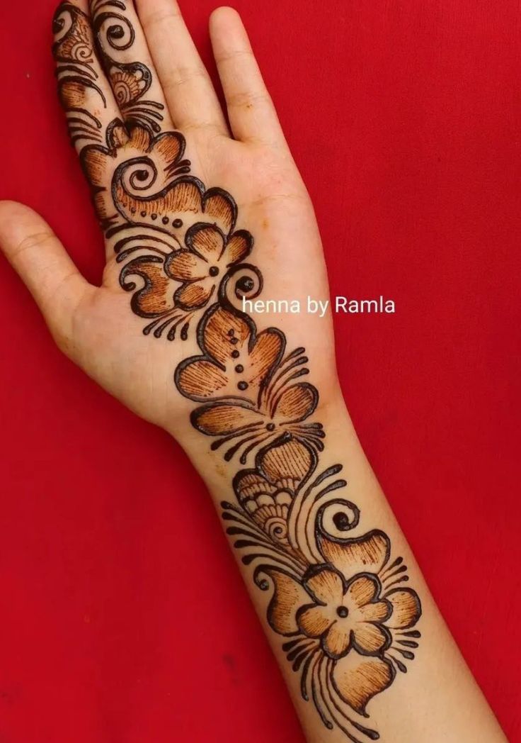 a woman's hand with henna tattoos on her arm and the palm is decorated with flowers