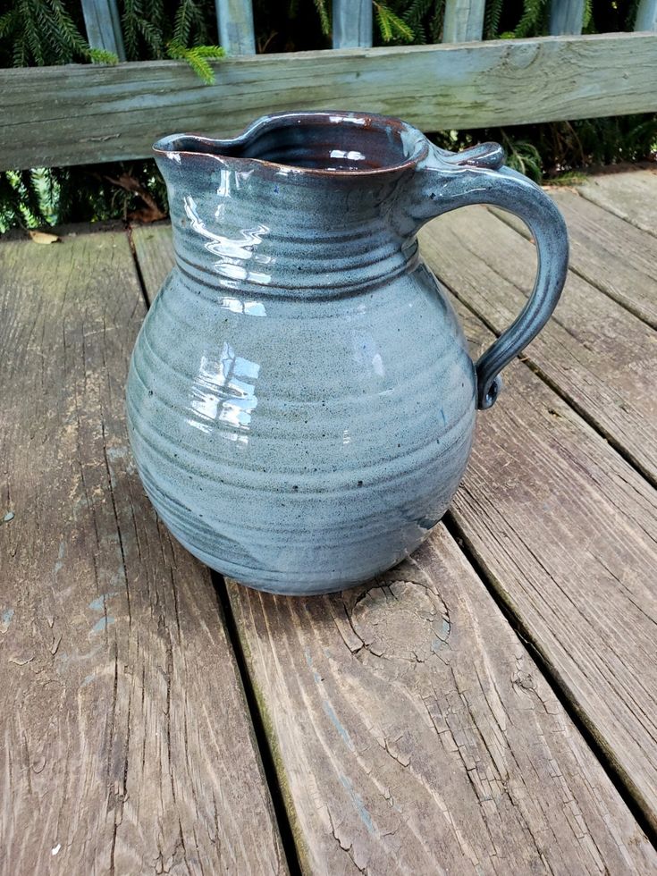 a blue vase sitting on top of a wooden table next to a fence and bushes