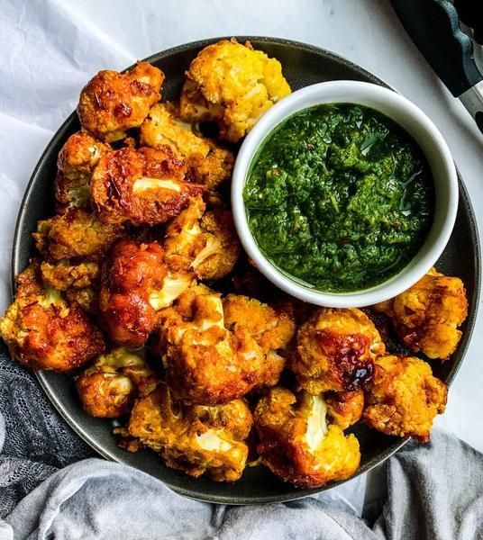 a plate filled with fried cauliflower next to a small bowl of pesto