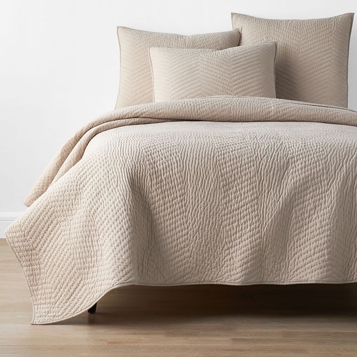 a bed with beige bedspread and pillows on top of wooden floor next to white wall