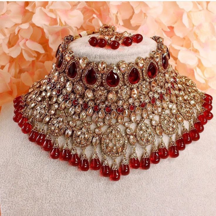 a red and white necklace is displayed on a mannequin with flowers in the background