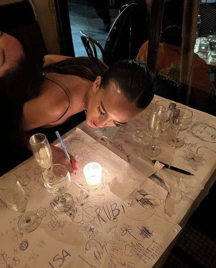 a woman sitting at a table in front of a lit candle with writing on it