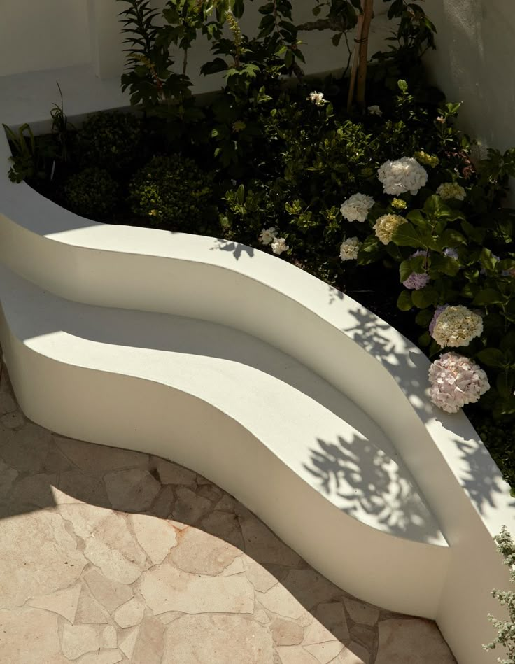 a white bench sitting next to a garden filled with flowers and greenery on the side of a building