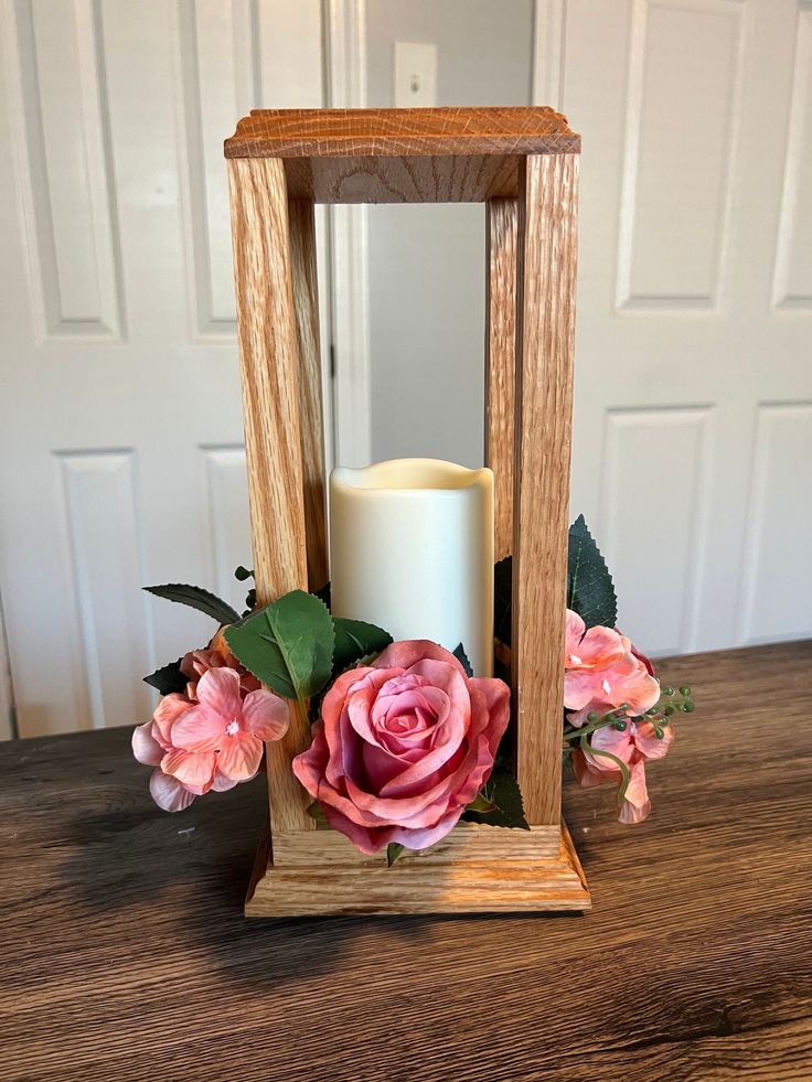 a wooden candle holder with pink flowers and greenery