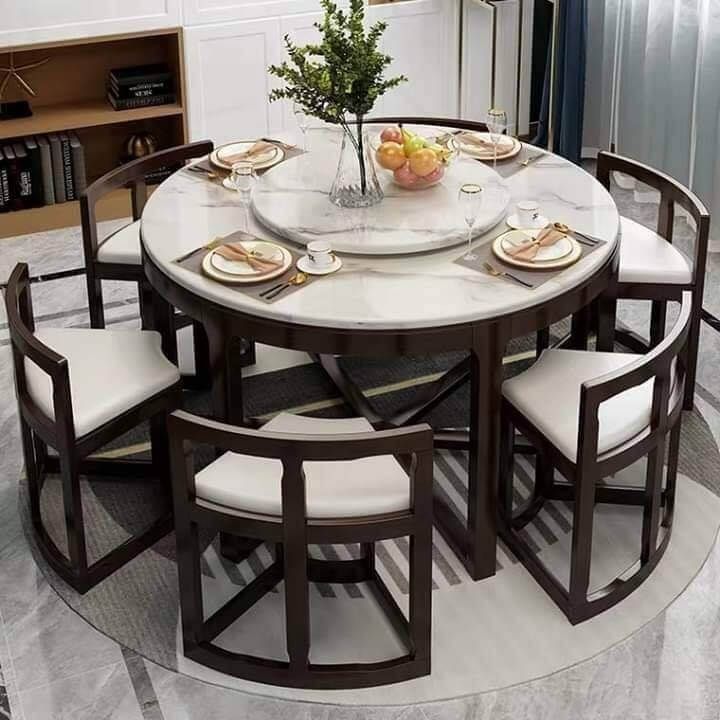 a round dining table with white chairs and plates on the top, surrounded by bookshelves