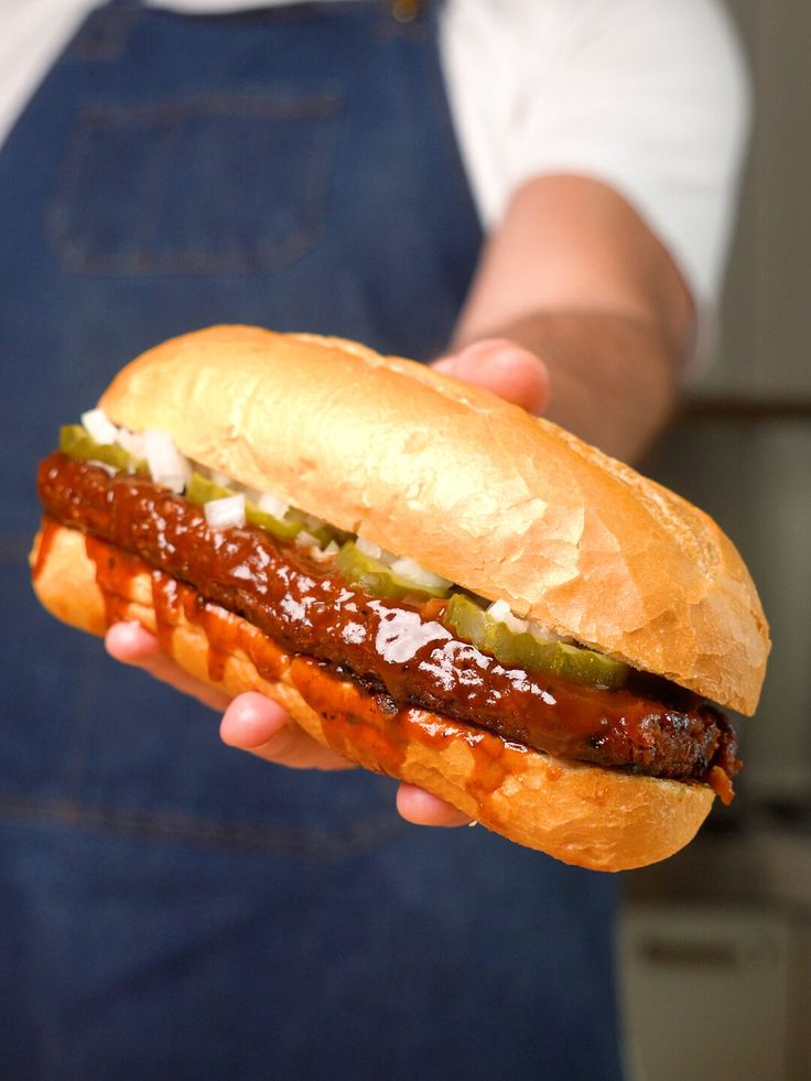 a person is holding a hot dog in their left hand and wearing an apron on the other side