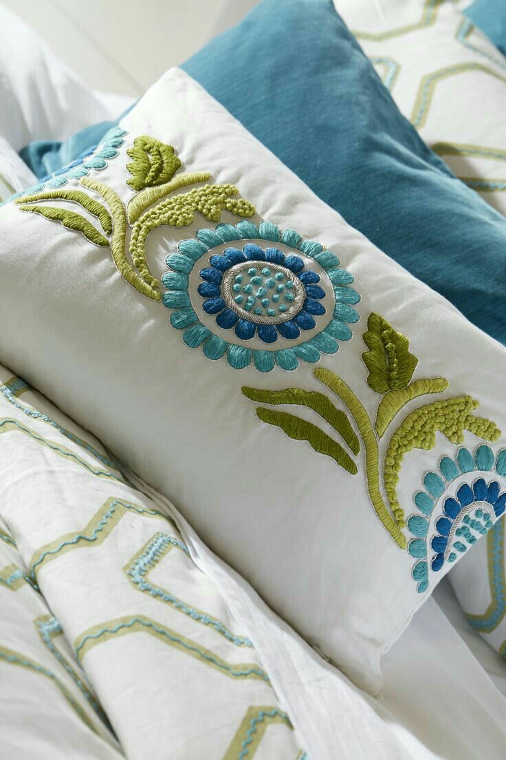 a bed with blue and green pillows on it's sides, along with a white comforter