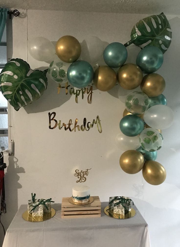 a birthday cake on a table with balloons and greenery in the shape of a wreath