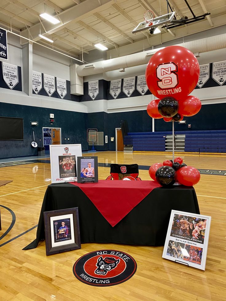 an indoor basketball court with balloons and pictures on the floor, in front of a table