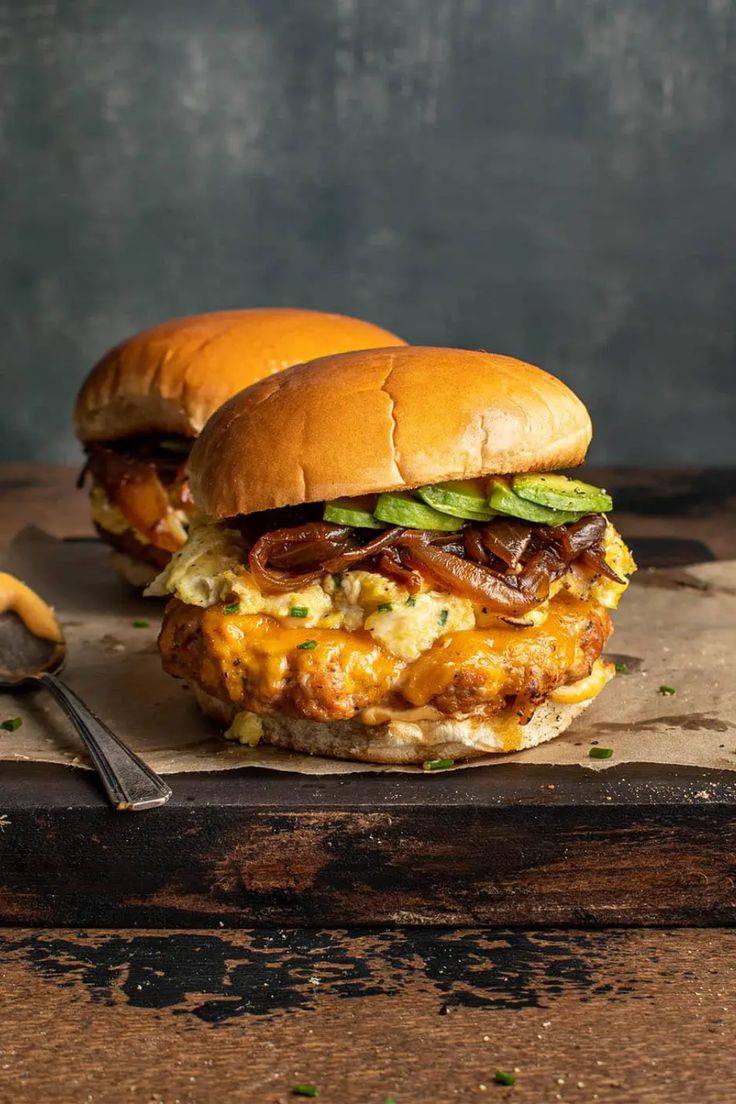 two burgers sitting on top of a cutting board next to a fork and knife