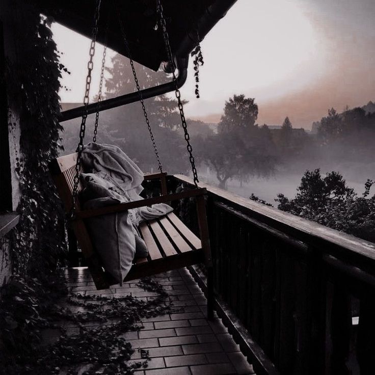 a person sitting on a porch swing in the foggy day with their head down