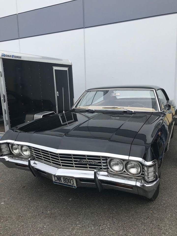 an old black car is parked in front of a white building with a trailer behind it