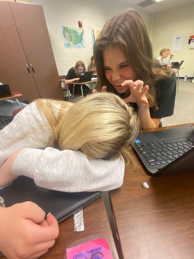 a woman is sitting at a desk with her head in the lap of another woman