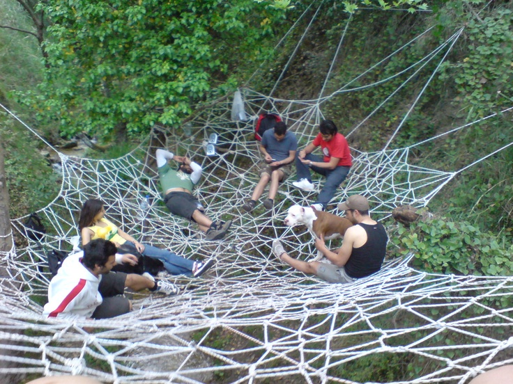 several people are sitting in a hammock on the side of a hill,