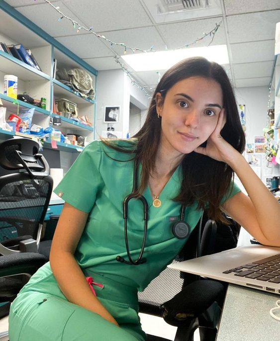 a woman in green scrubs sitting at a desk with a laptop computer on her lap