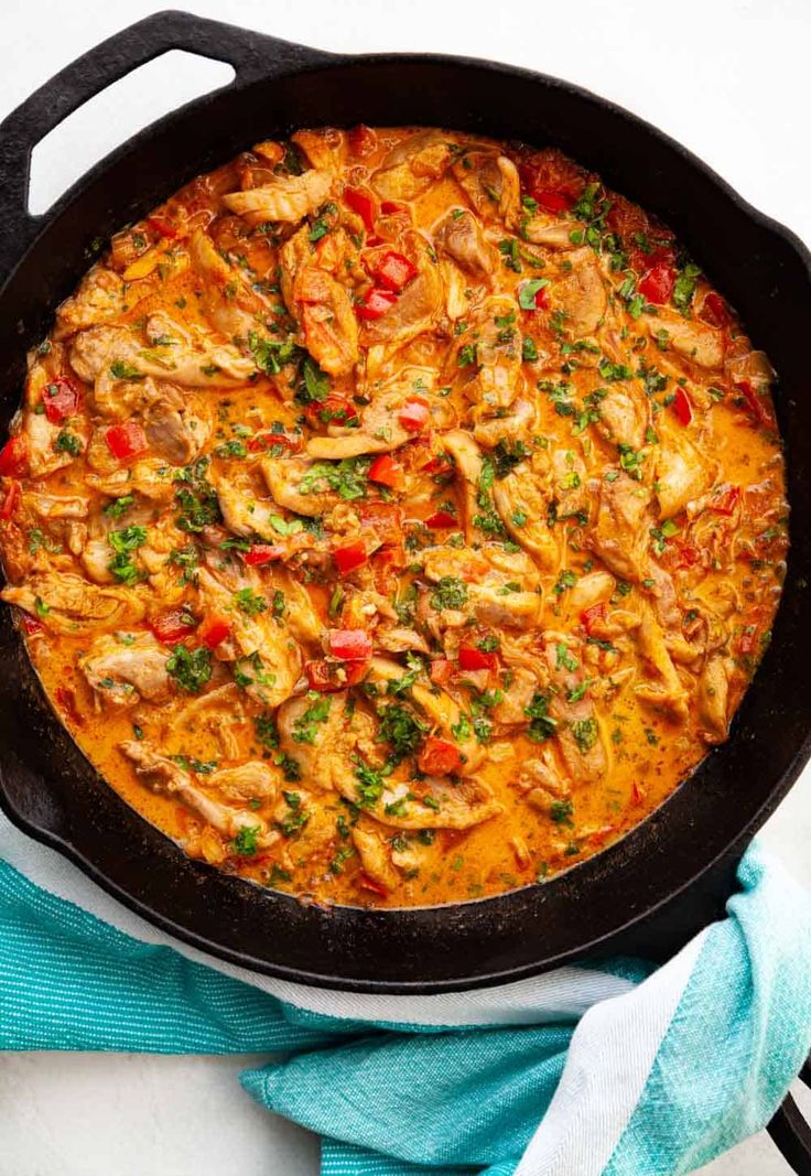 a skillet filled with chicken and vegetables on top of a blue towel next to a fork