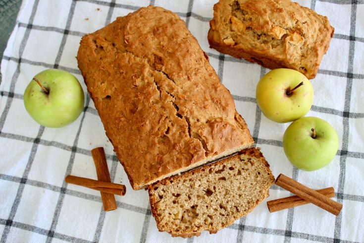 sliced loaf of bread sitting on top of a towel next to apples and cinnamon sticks