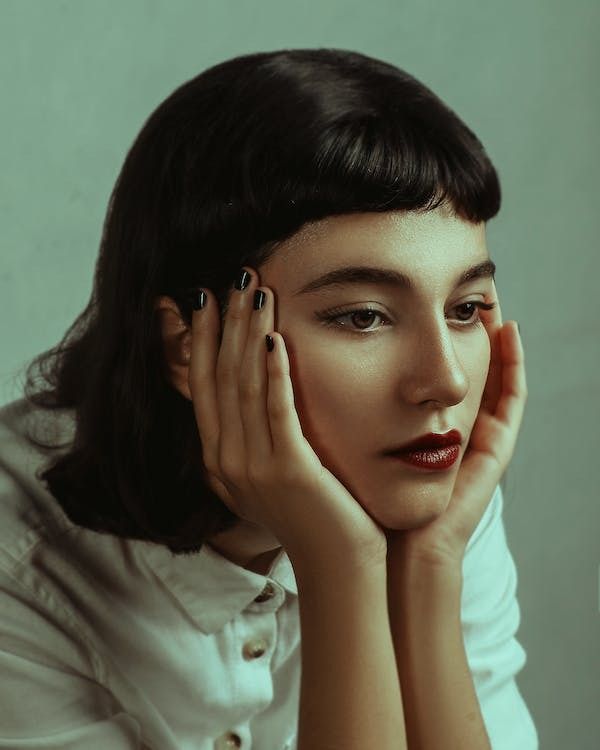 a woman with her hands on her face, posing for the camera and holding her hand near her face