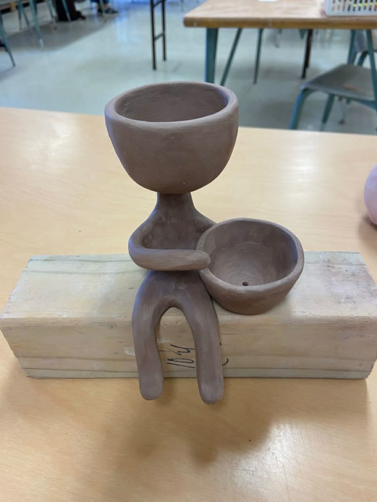 a clay sculpture sitting on top of a wooden table next to a bowl and spoon