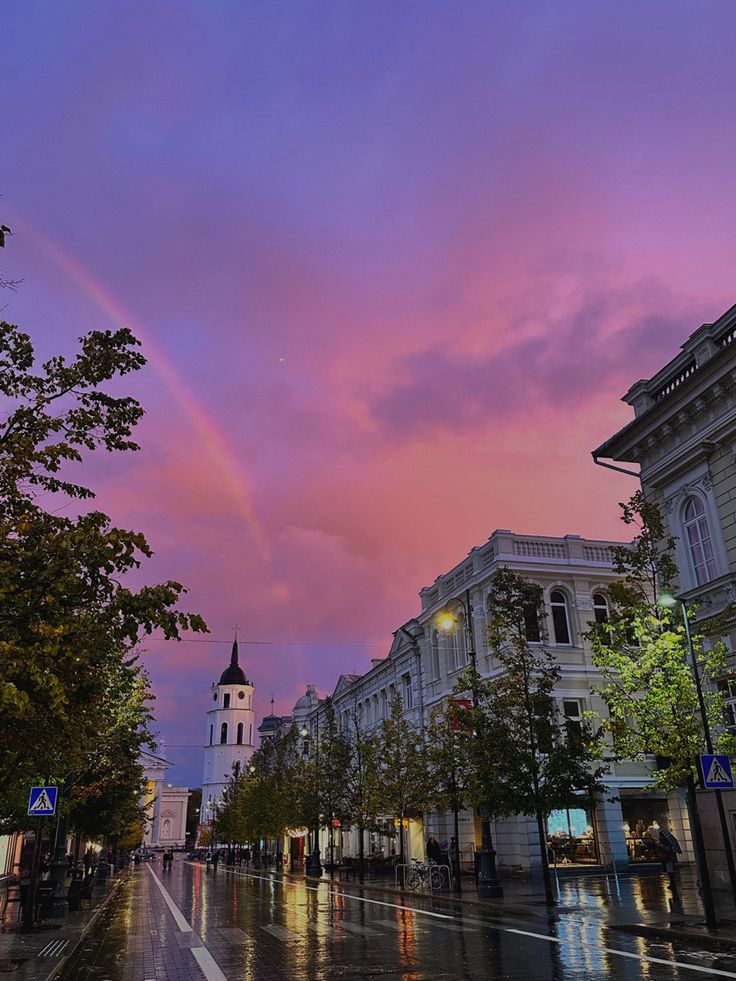 a city street with buildings and a rainbow in the sky