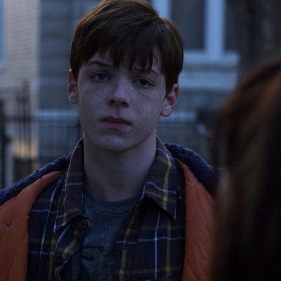 a young man with freckles on his face standing in front of a building