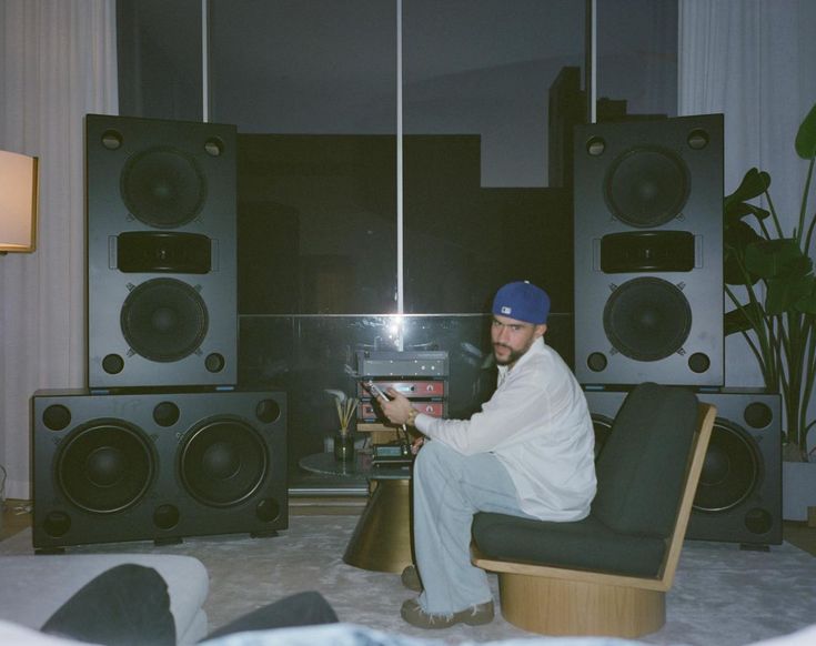 a man is sitting on a chair in front of some speakers and a table with a remote control