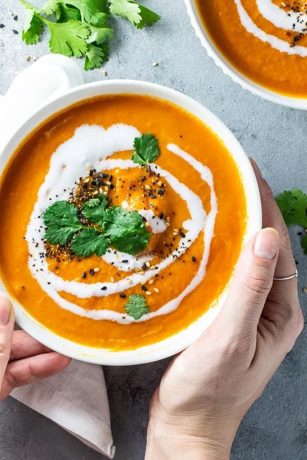 two hands holding a bowl of carrot soup